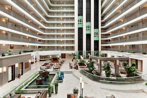 Un vestíbulo de hotel de varios niveles con un patio central, múltiples balcones y zonas de estar interiores.