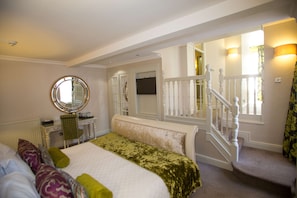 Relax in a spacious room with a large bed, seating area, and desk, featuring a round mirror and staircase.