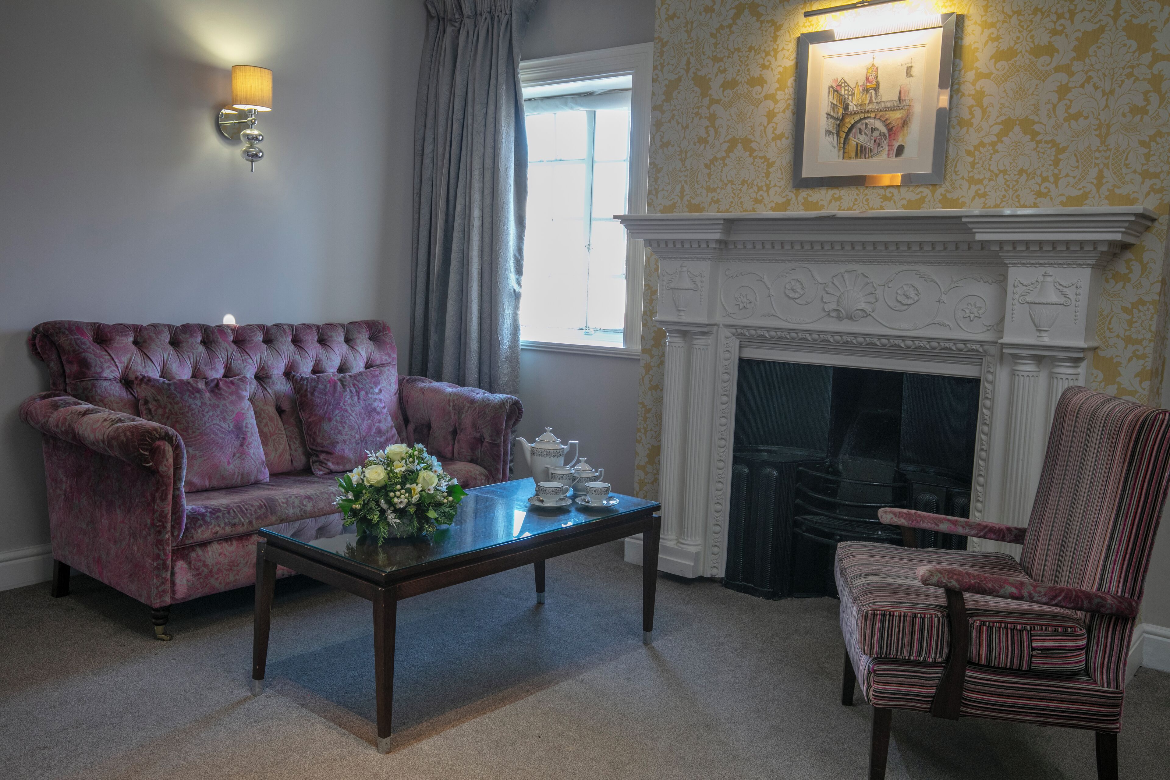 A living room with a tufted sofa, a striped armchair, a coffee table with a vase of flowers, and a fireplace.
