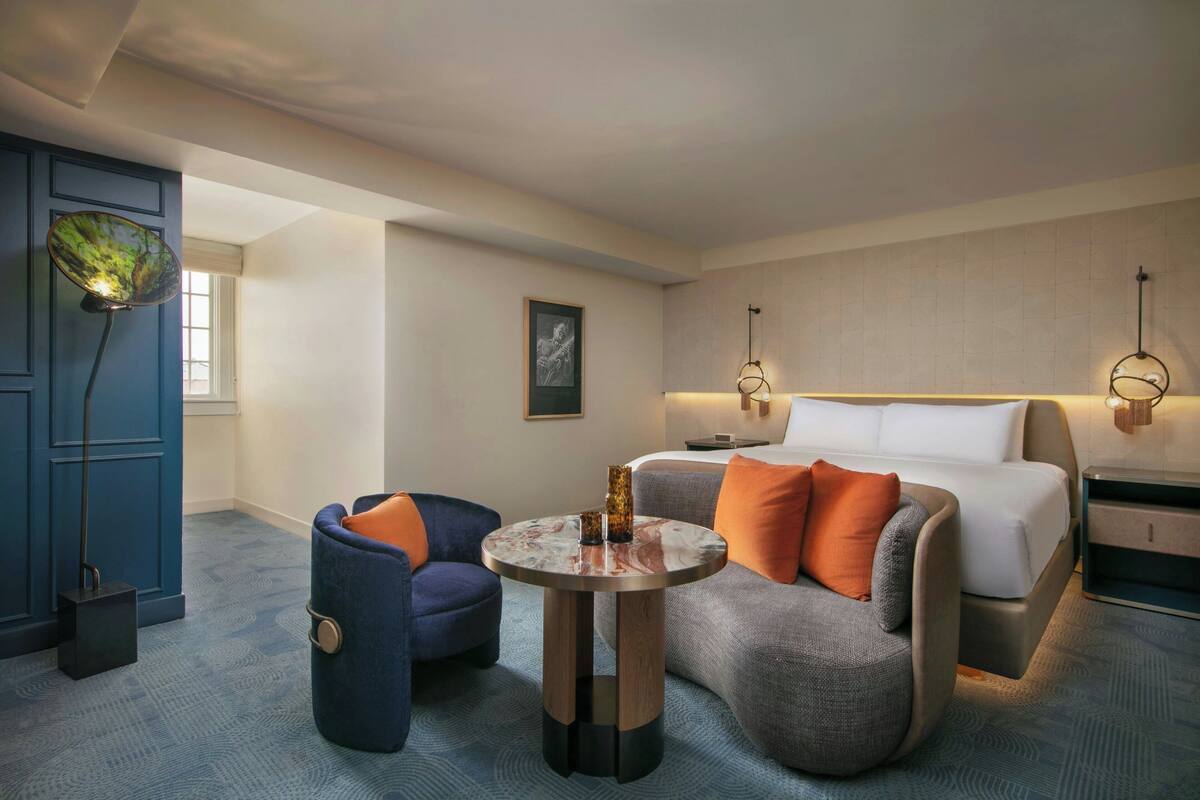 A modern hotel room with a bed, two armchairs, a side table, and a large mirror.