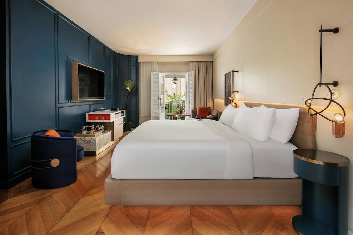 A hotel room with a large bed, a TV, a desk with a computer, and a view of the outdoors.