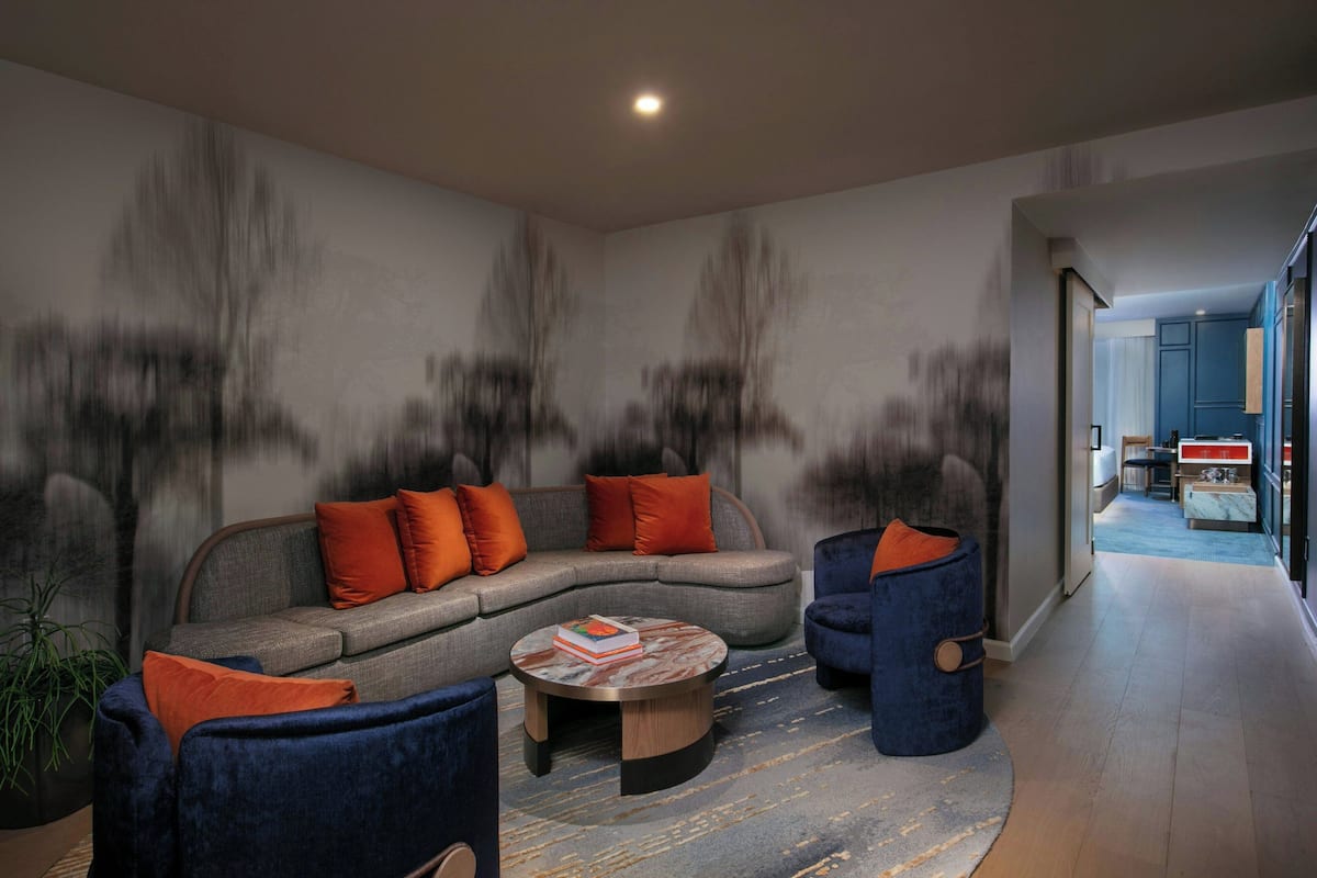 A modern living room with a grey sectional sofa, blue armchairs, and a round coffee table with books.