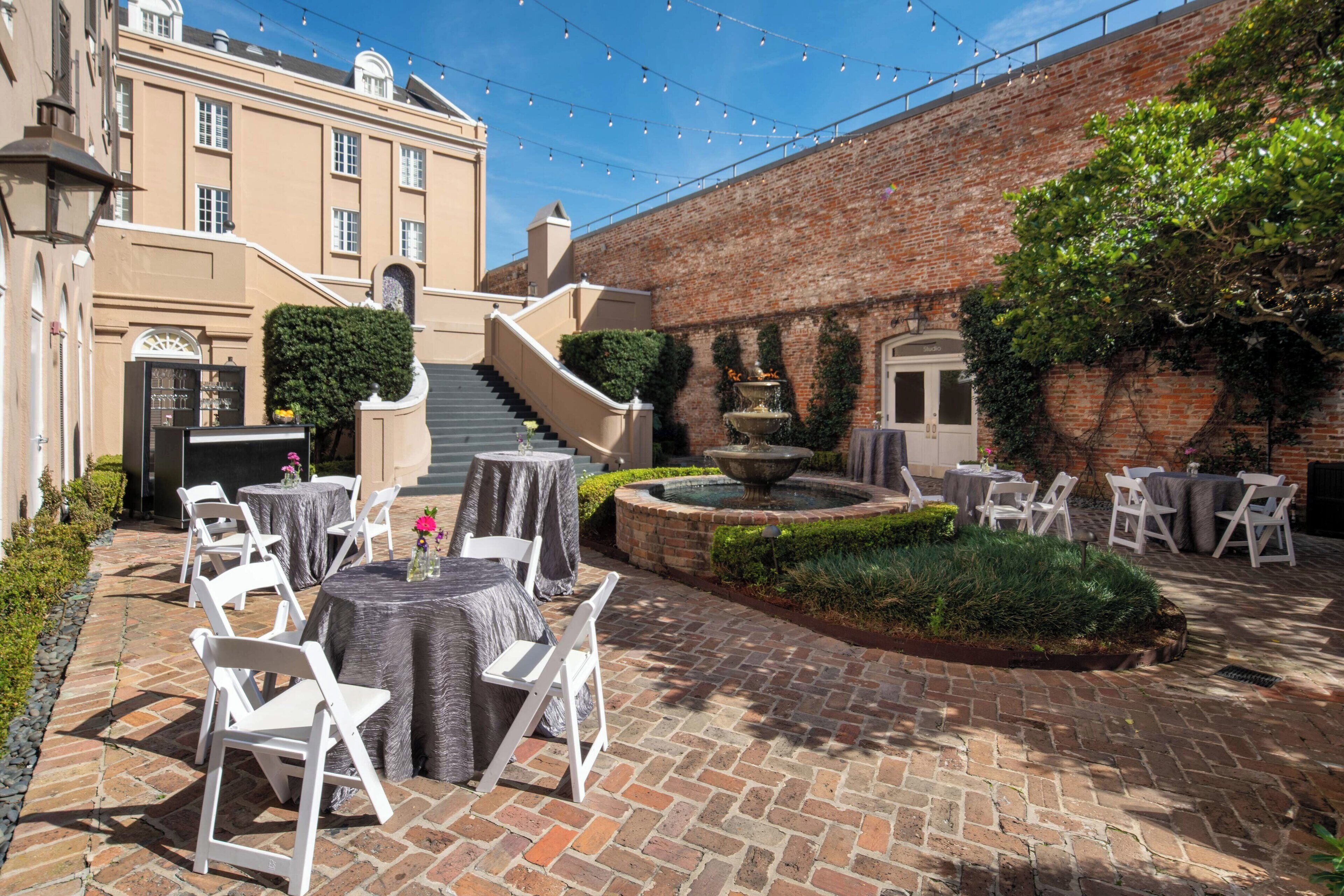A courtyard with outdoor seating, a fountain, and a brick building with a staircase.