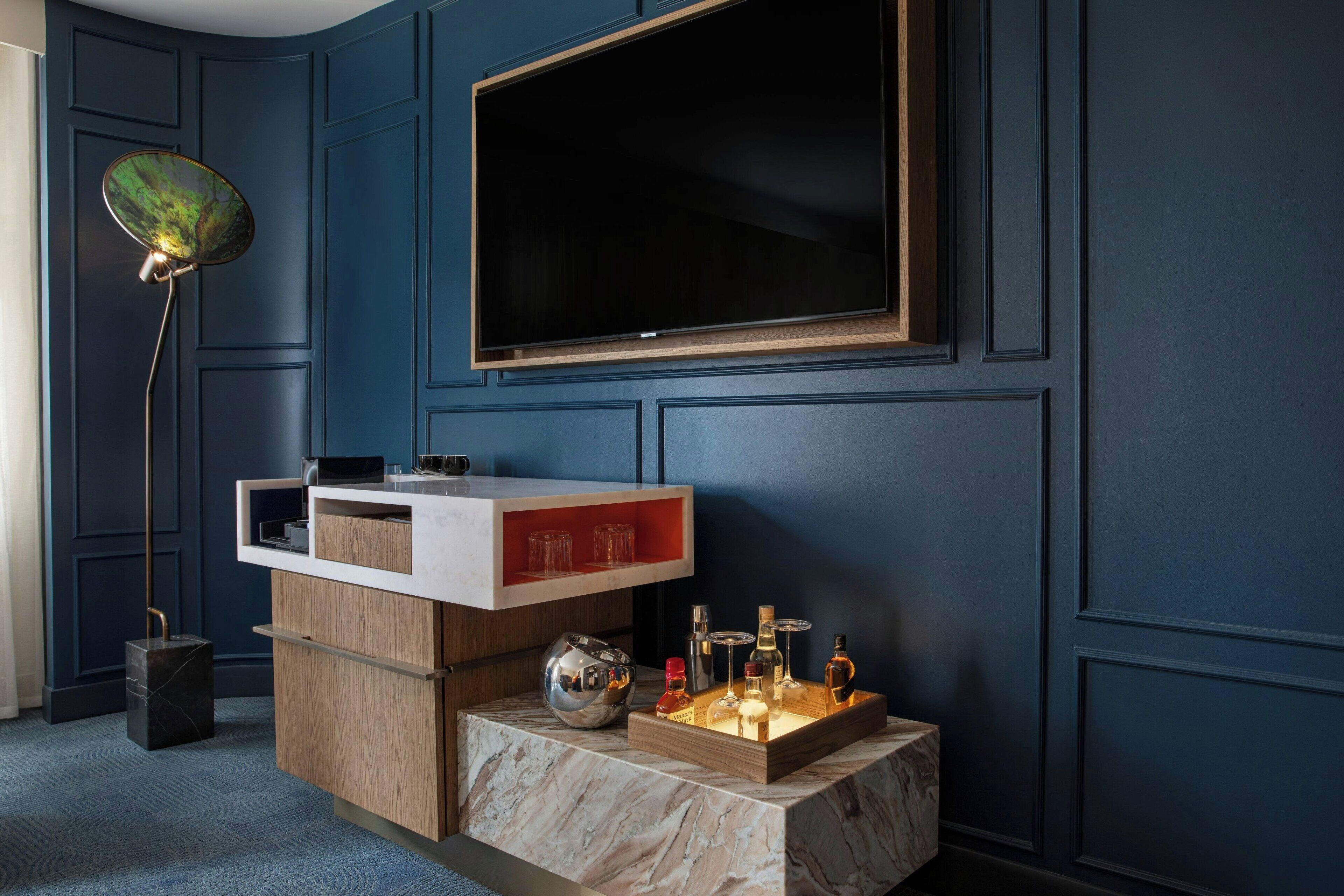 Een moderne woonkamer met een donkerblauwe muur, een grote flatscreen televisie bevestigd boven een houten console tafel, en een vloerlamp aan de linkerkant.