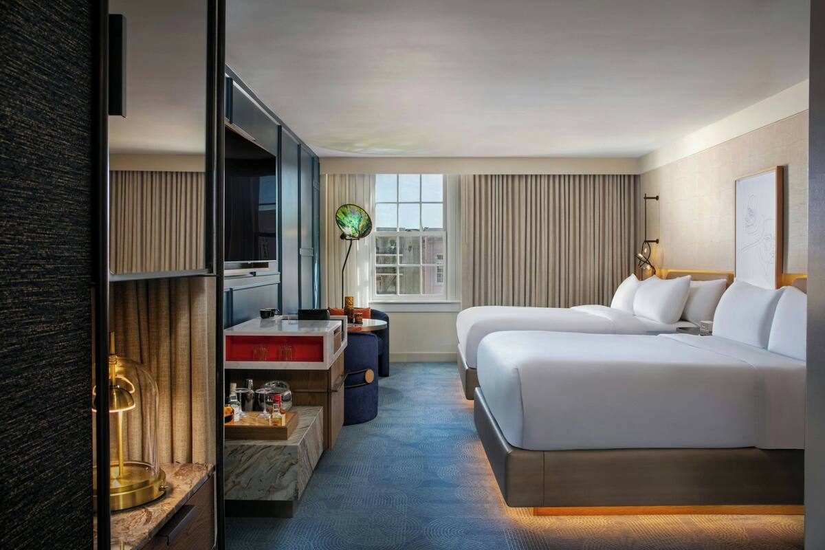 A hotel room with a bed, a desk with a TV, a lamp, and a window with curtains.