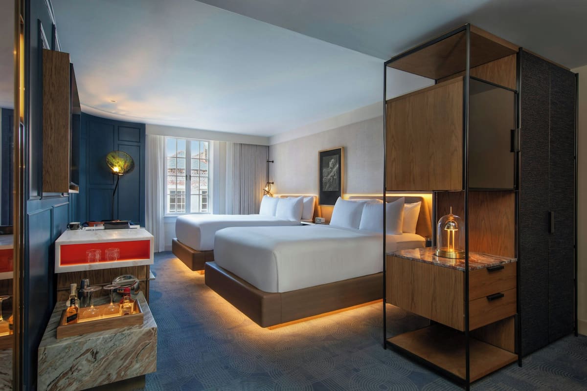 A hotel room with a large bed, a desk with a lamp, a wardrobe, and a view of the city through the window.