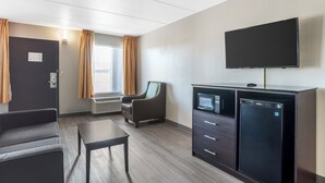 A hotel room with a flat-screen TV, a minibar, a sofa, a table, and a window with curtains. - Quality Inn Simpsonville - Greenville (Simpsonville)