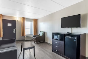 A hotel room with a flat-screen TV, a minibar, a sofa, a table, and a window with curtains. - Quality Inn Simpsonville - Greenville (Simpsonville)
