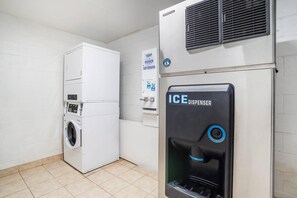 A laundry room with a stacked washer and dryer, an ice dispenser, and a sign for softeners. - Quality Inn Simpsonville - Greenville (Simpsonville)