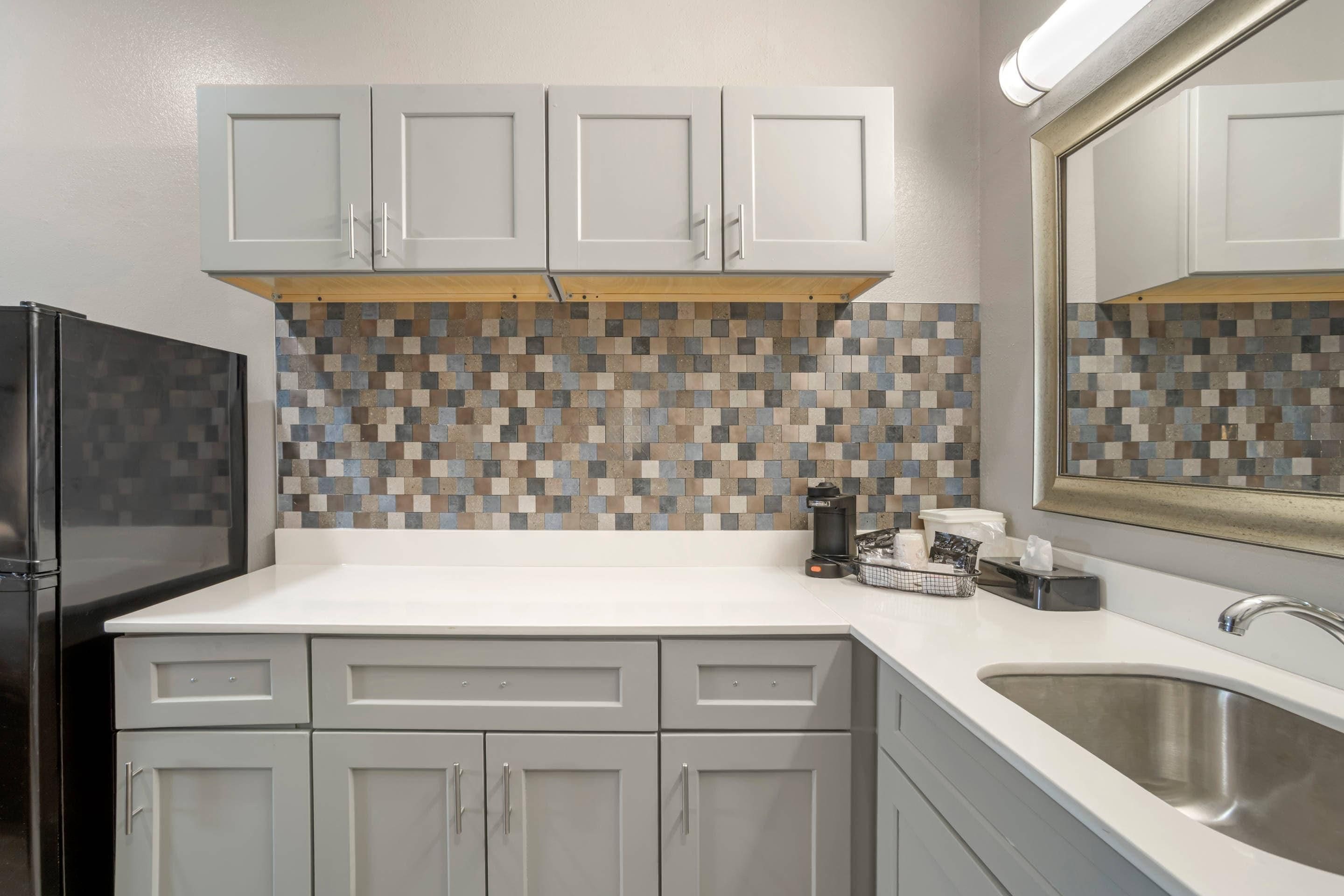 Una cocina moderna con armarios blancos, un protector contra salpicaduras de azulejos, un refrigerador negro y un lavamanos de acero inoxidable.