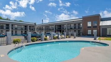 A swimming pool with a 4 ft depth, surrounded by a building with multiple balconies and a parking area.