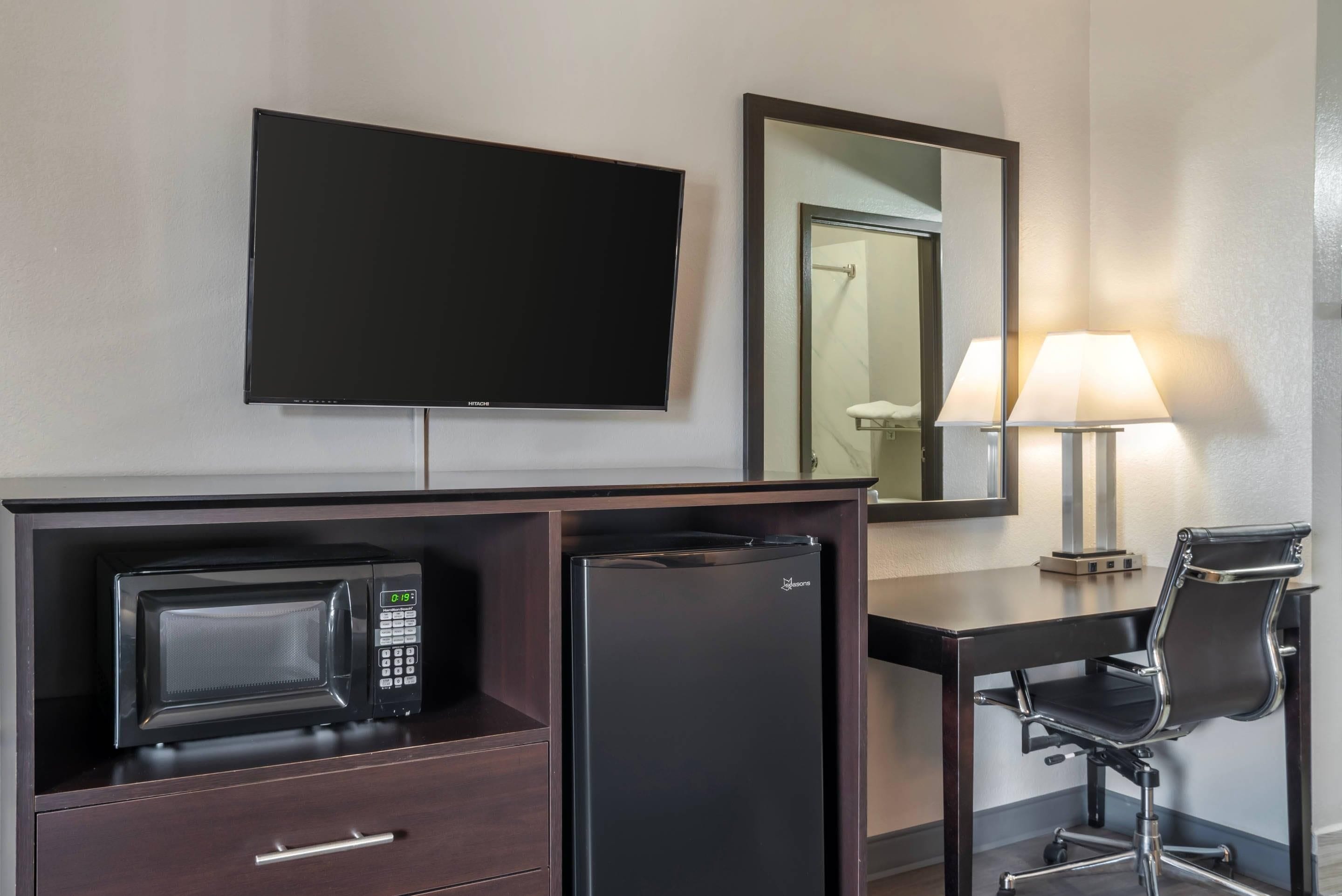 Habitación de hotel con televisor de pantalla plana, minibar, escritorio con silla y lámpara.