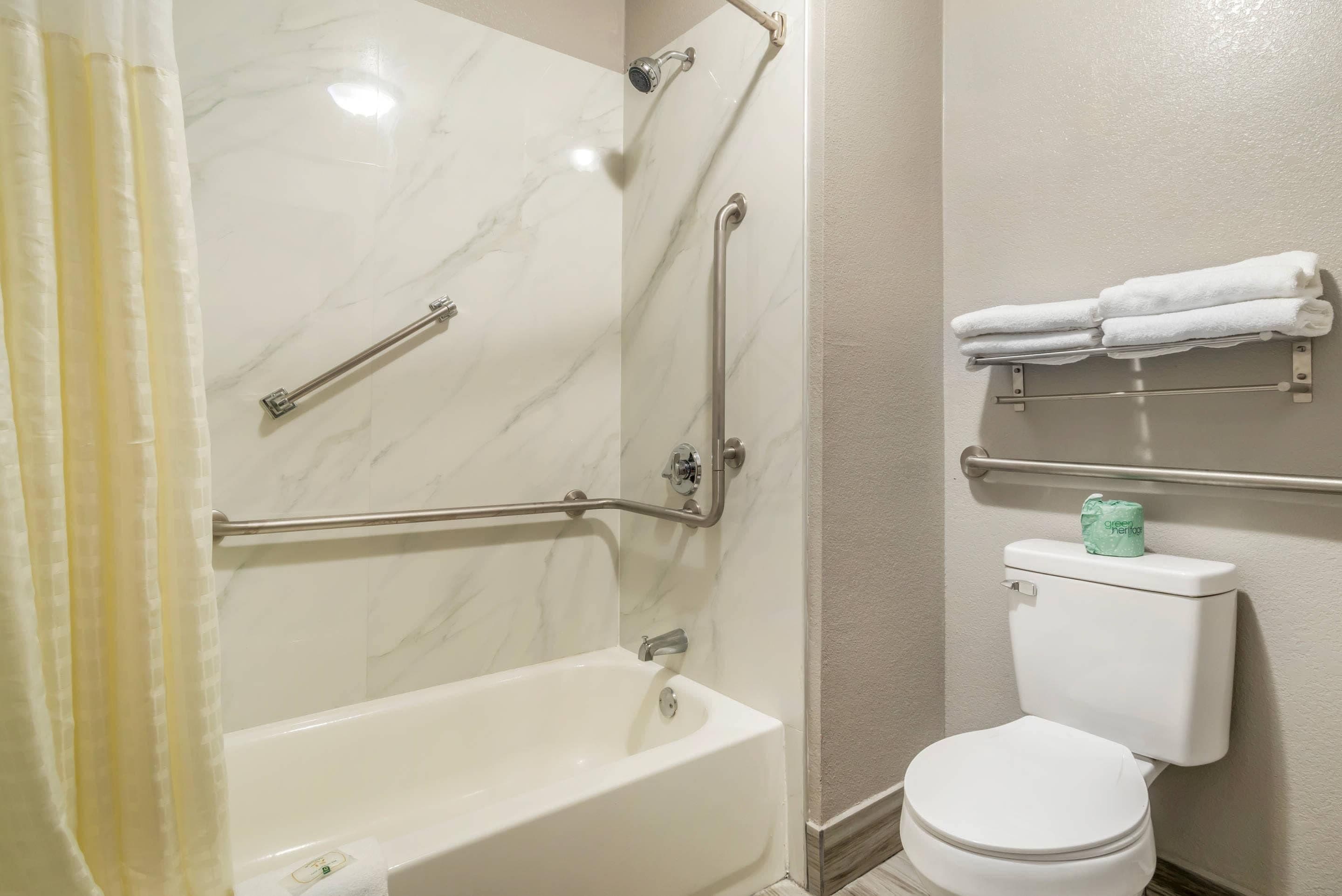 A bathroom with a bathtub, toilet, and handrails.