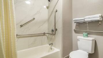 A bathroom with a bathtub, toilet, and handrails.
