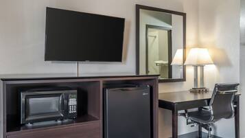 Ein Hotelzimmer mit Flachbildfernseher, Minibar, Schreibtisch mit Stuhl und einer Lampe.