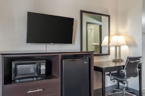A hotel room with a flat-screen TV, a minibar, a desk with a chair, and a lamp. - Quality Inn Simpsonville - Greenville (Simpsonville)