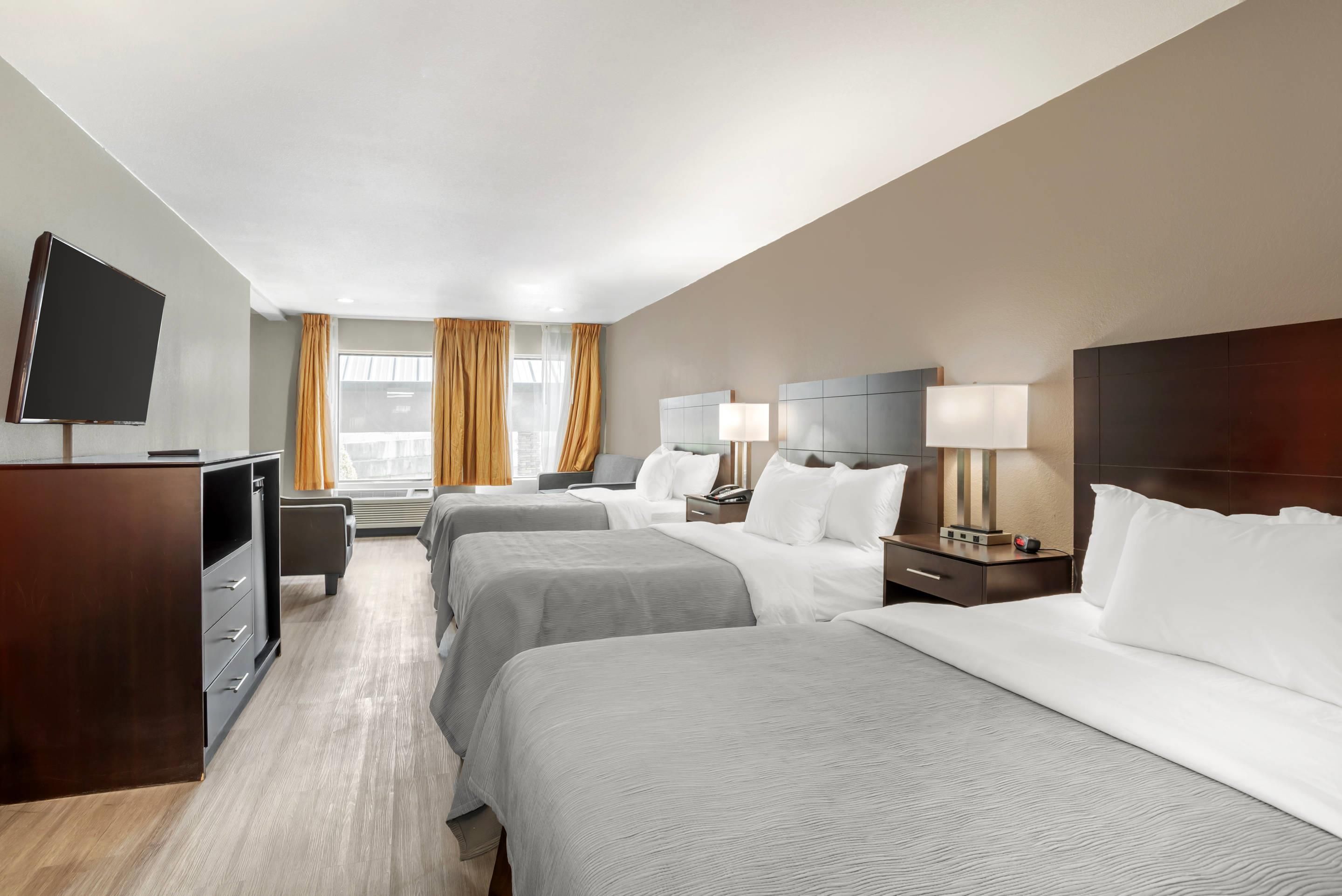 Habitación de hotel con dos camas, un escritorio, un televisor y una ventana con cortinas.