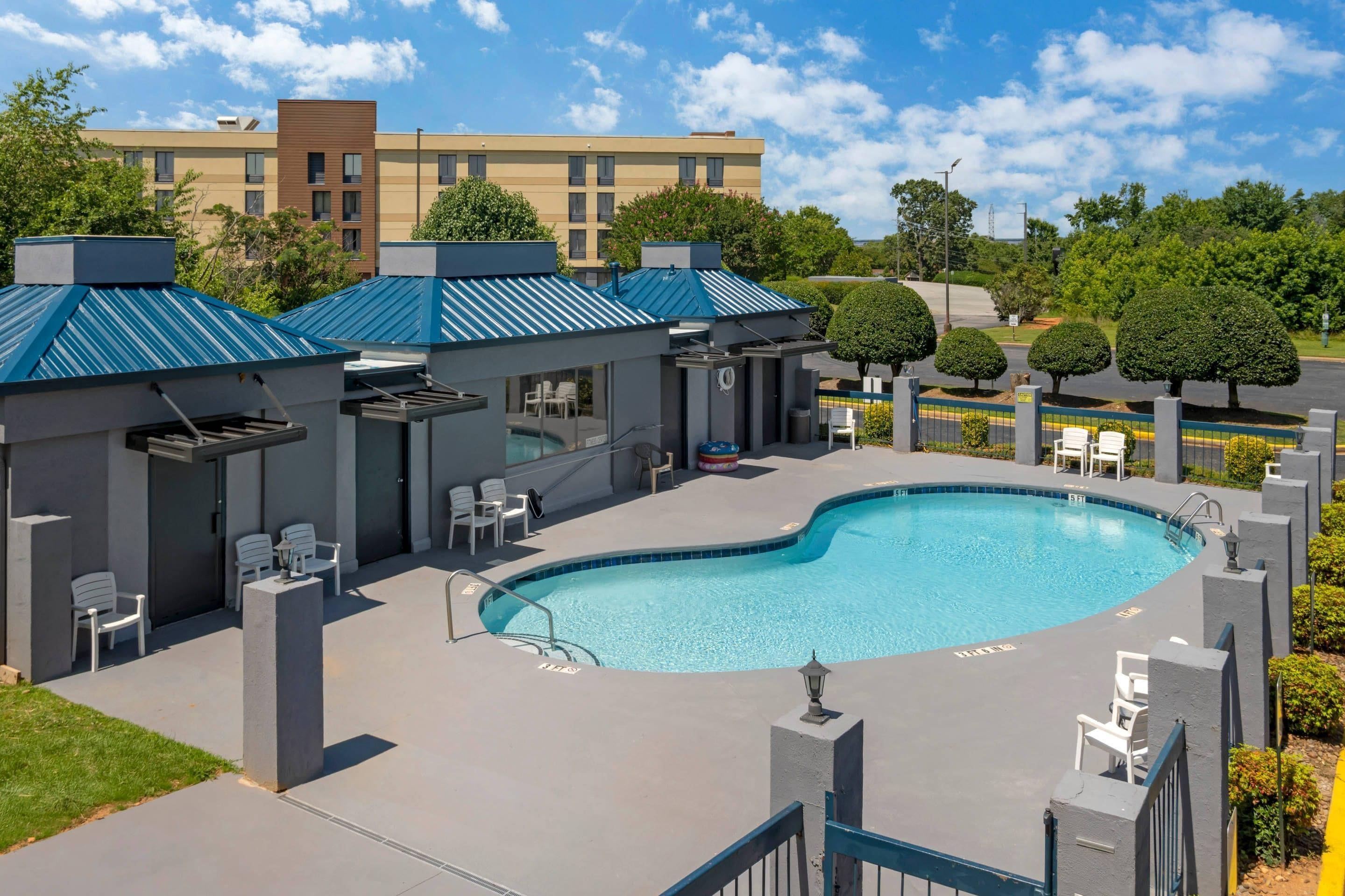 A swimming pool area with a pool, lounge chairs, and a building with a blue roof.