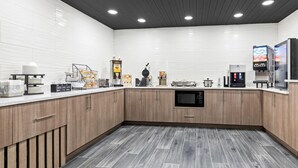A modern kitchen with wooden cabinets, a microwave, a waffle maker, and a coffee machine. - Super 8 by Wyndham Athens (Athens)