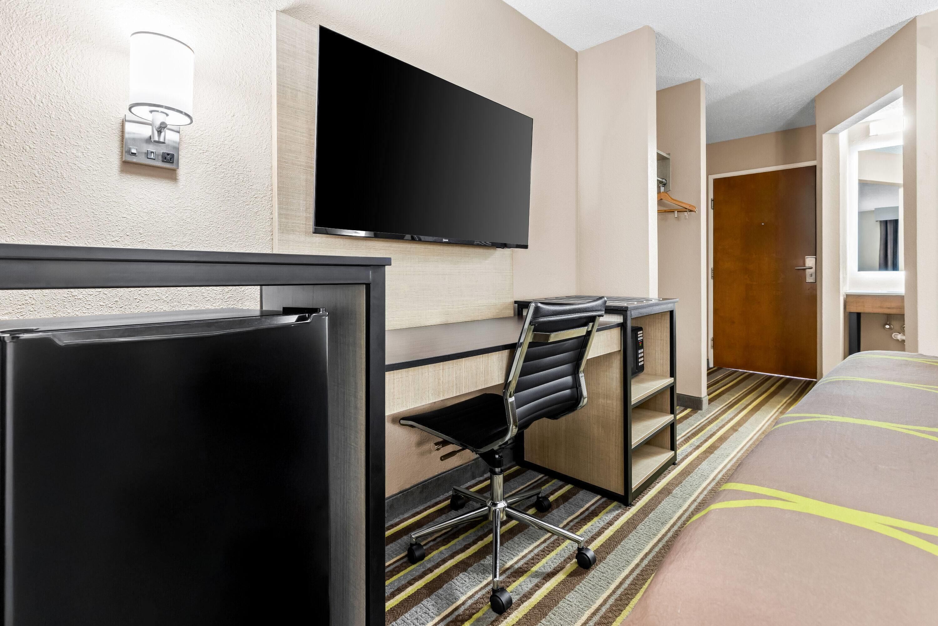 Quarto de hotel com cama, escrivaninha, cadeira, televisão e minibar.