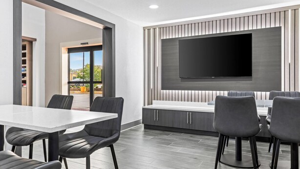 A modern dining area with a large flat-screen TV mounted on the wall, a white table, and black chairs. - Super 8 by Wyndham Athens (Athens)