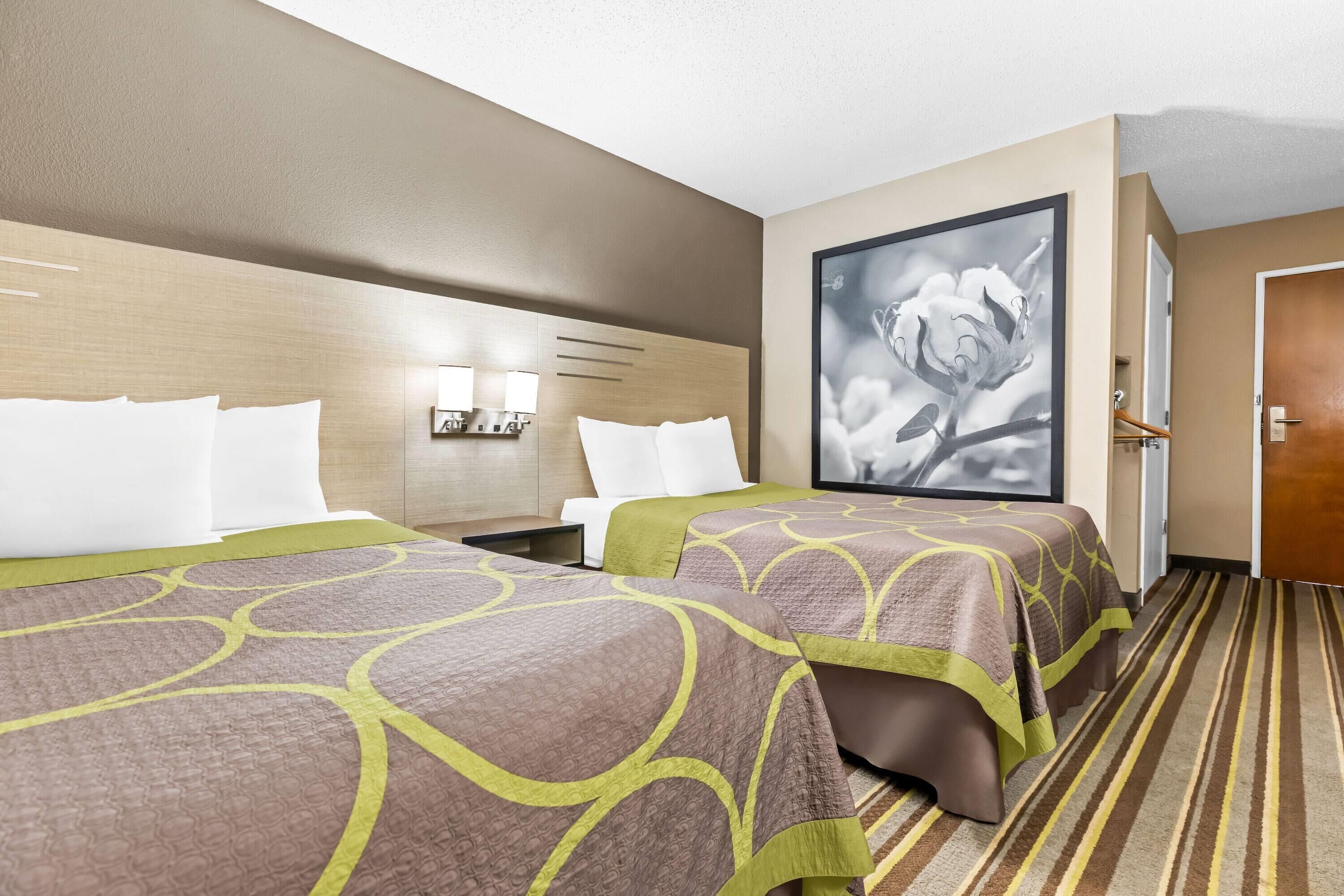 A hotel room with two beds, a large framed picture on the wall, and a striped carpet.