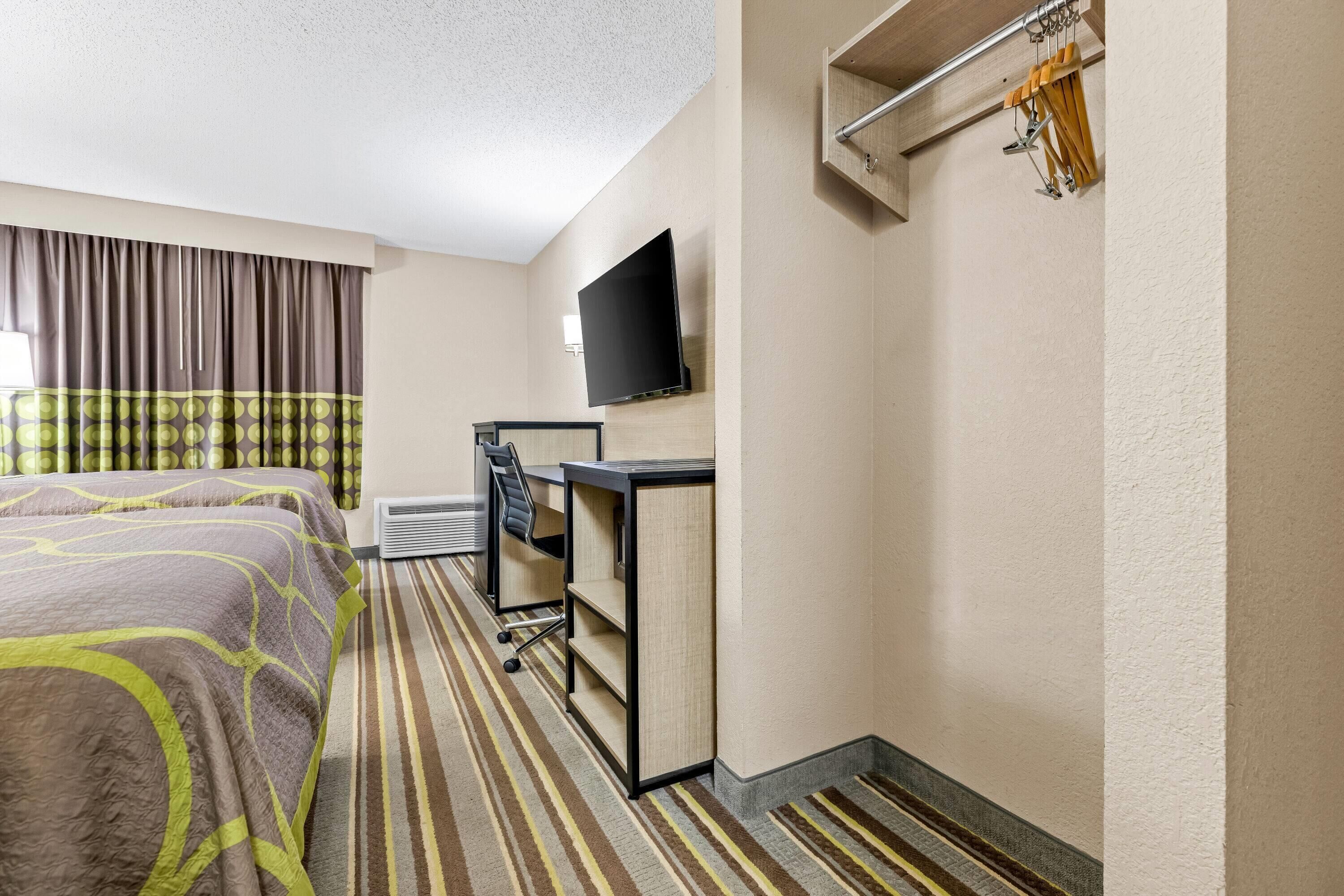 A hotel room with two beds, a desk, a chair, a flat-screen TV, and a coat rack.