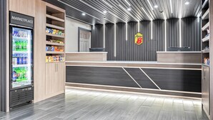 A modern reception area with a 'MARKETPLACE' refrigerator stocked with beverages, a 'Super 8' sign, and a clean, tiled floor. - Super 8 by Wyndham Athens (Athens)