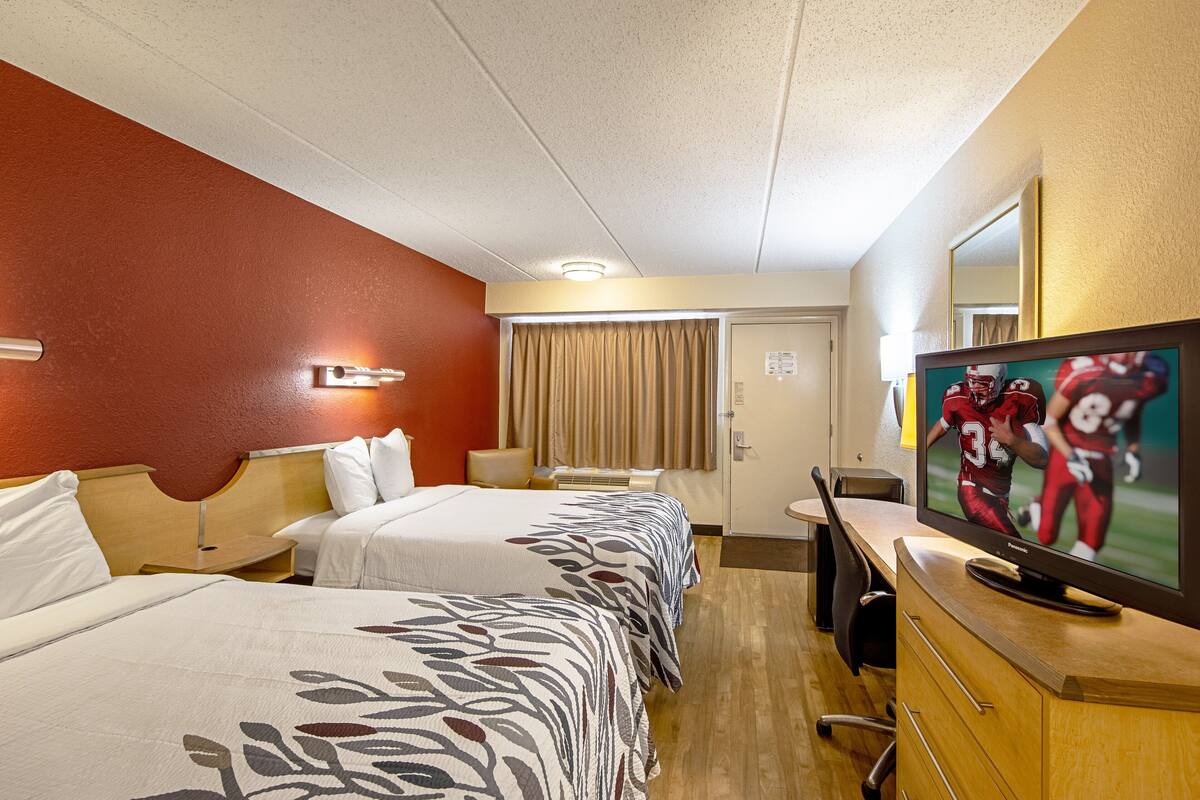 A hotel room with two beds, a television, a desk, and a mirror.