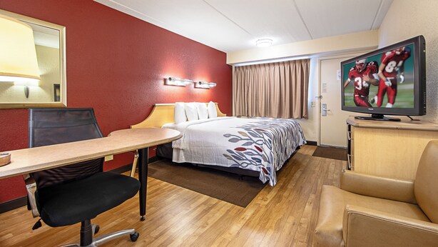 Una habitación de hotel con cama, escritorio, silla, televisor y ventana con cortinas.