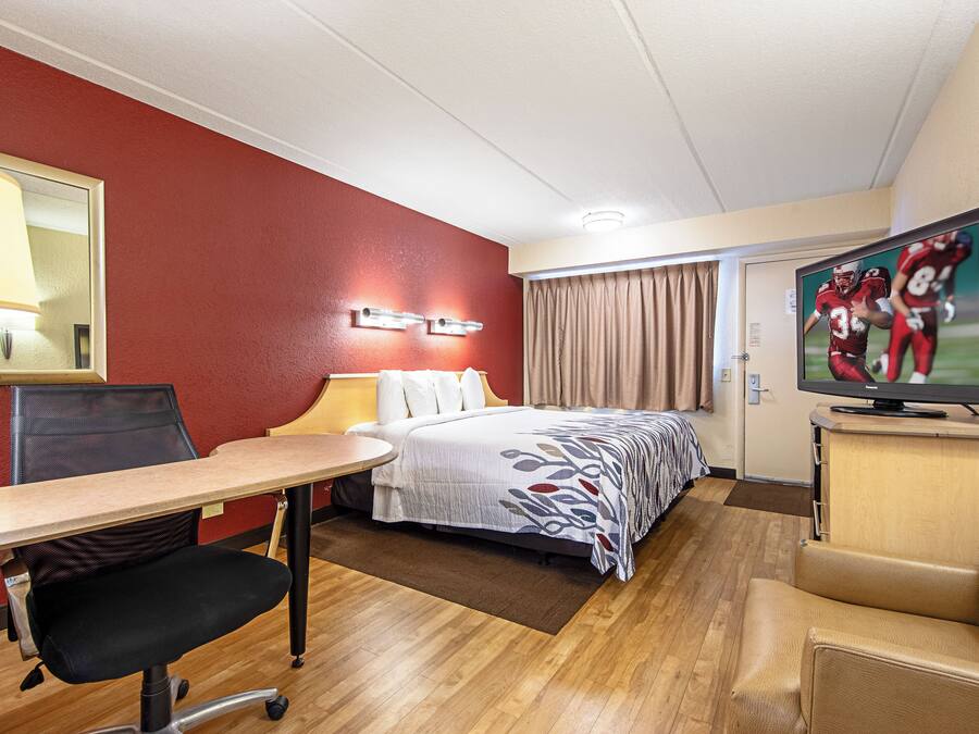 Una habitación de hotel con cama, escritorio, silla, televisor y ventana con cortinas.