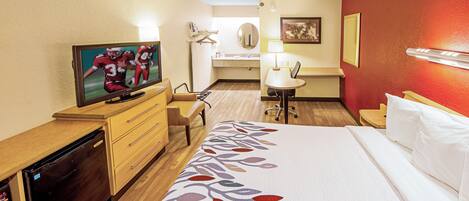 Una habitación de hotel con cama, escritorio con televisor, baño y zona de comedor.