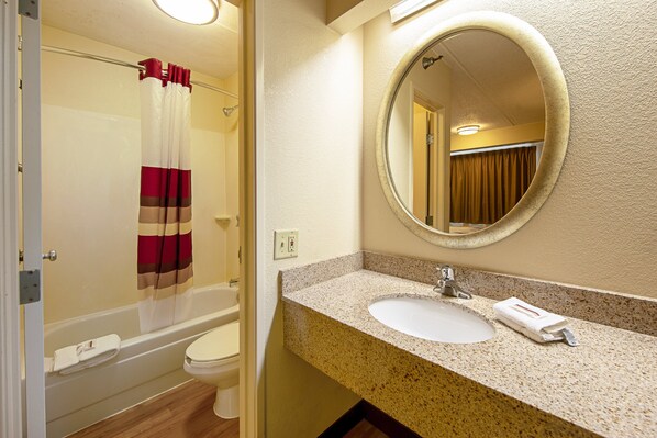 A bathroom with a shower, toilet, sink, and a round mirror. - Red Roof Inn Charleston - Kanawha City, WV (Charleston)