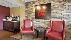 Ein Empfangsbereich eines Red Roof Inn mit einer Steinwand, zwei Ledersesseln, einem kleinen Tisch und einer Kaffeestation.