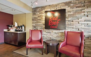A Red Roof Inn reception area with a stone wall, two leather chairs, a small table, and a coffee station. - Red Roof Inn Charleston - Kanawha City, WV (Charleston)
