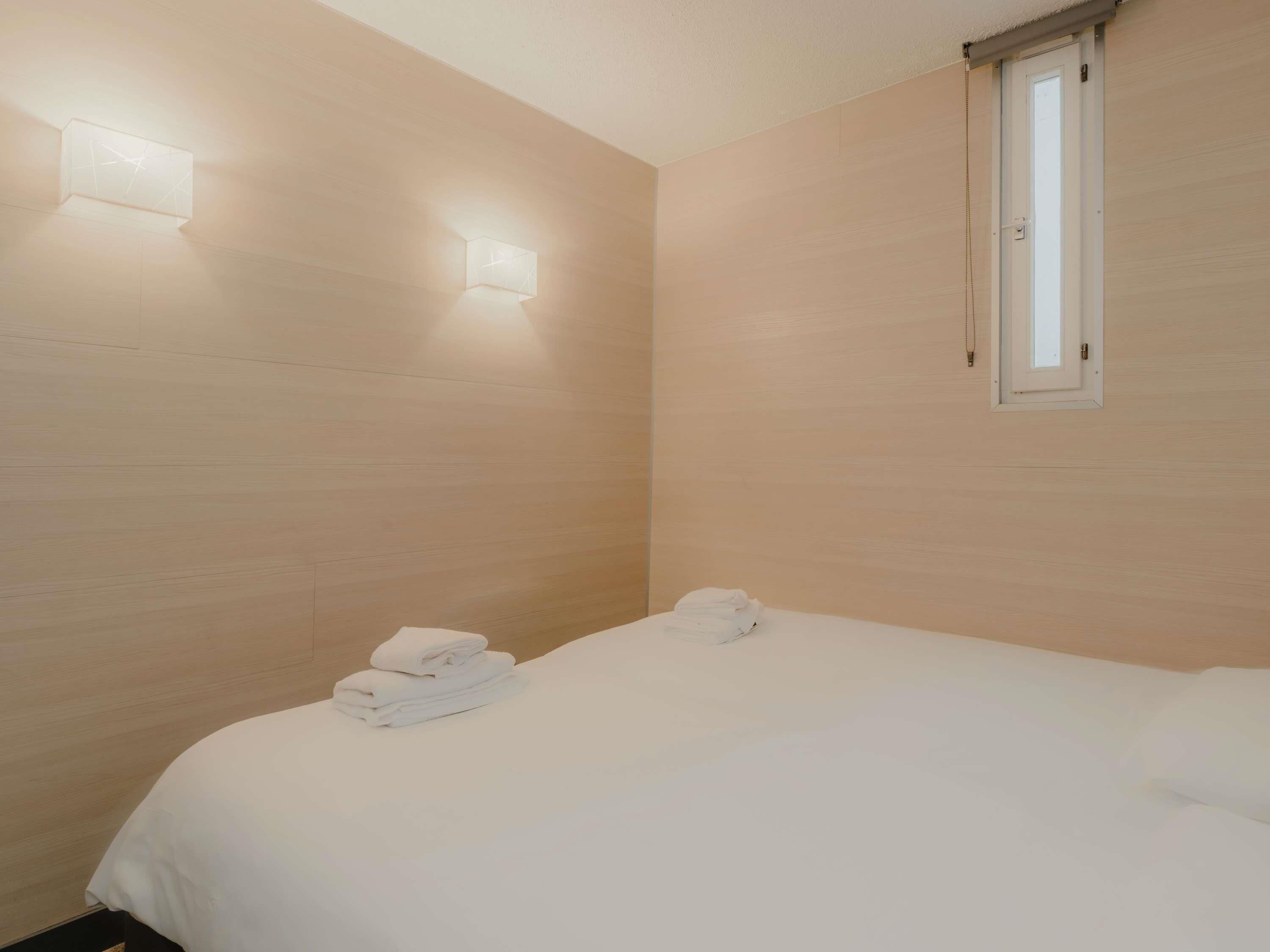 A hotel room with a bed, a window, and wall-mounted lights.
