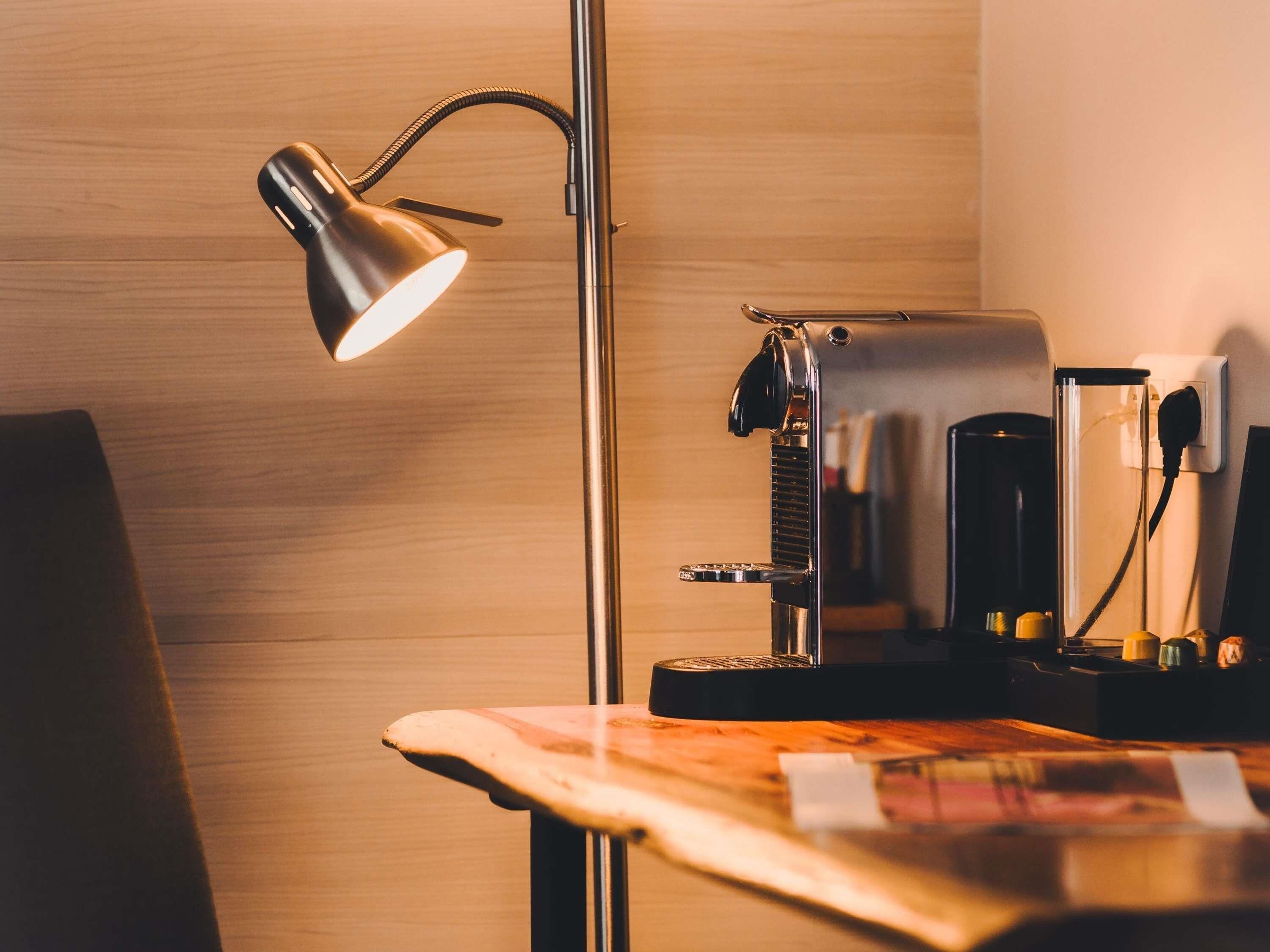 A desk with a lamp, a coffee machine, and a power outlet.