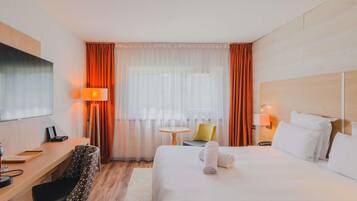A hotel room with a bed, a desk, a chair, a TV, and a window with curtains.