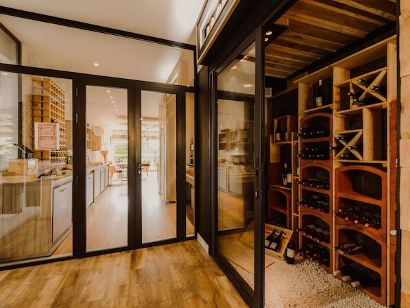 A modern interior with a wine cellar, wooden flooring, and glass doors leading to a dining area.