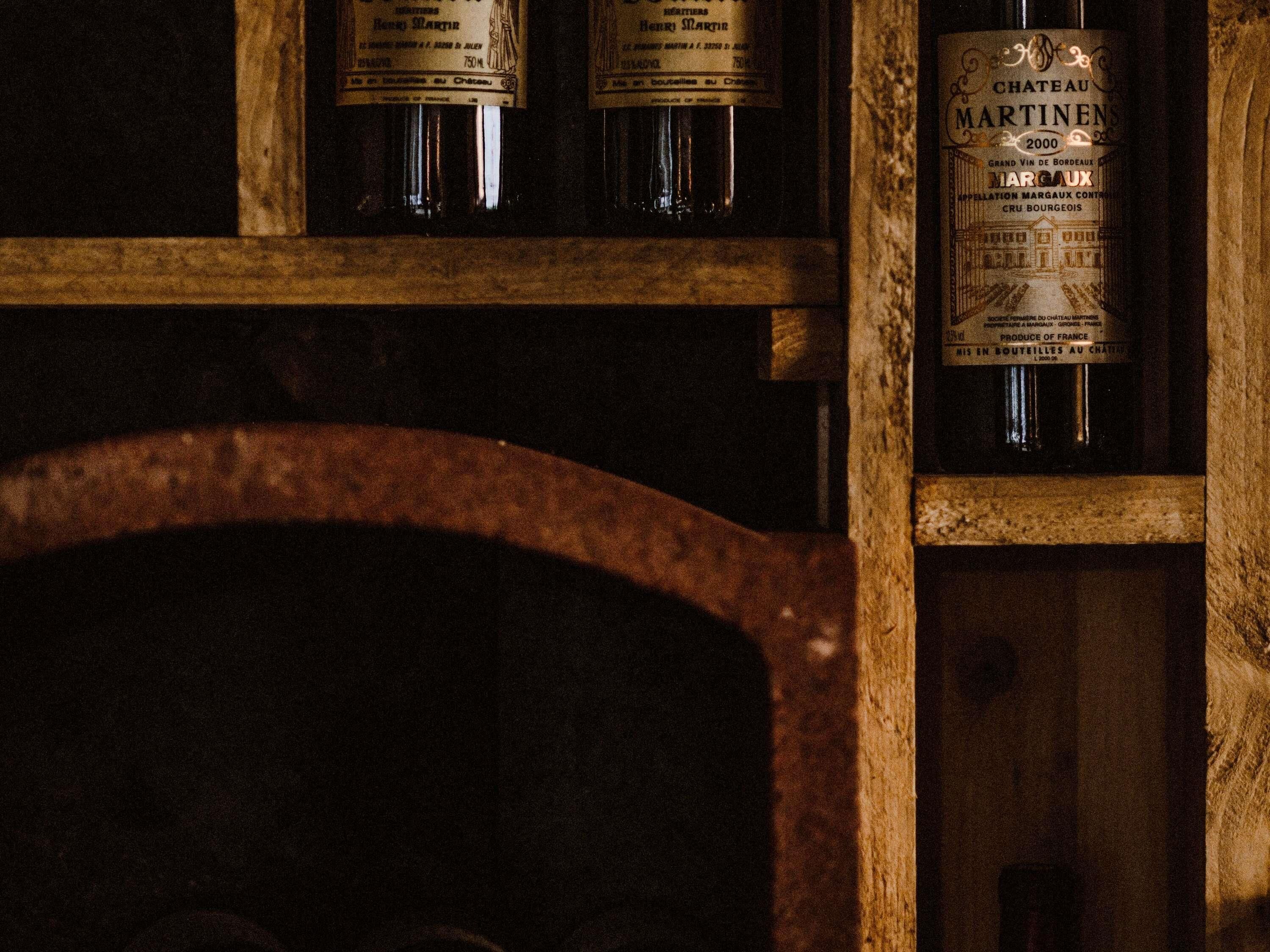 A wooden shelf with bottles of Chateau Martinens Margaux wine from 2000, a vintage wine bottle with a label featuring a chateau illustration.