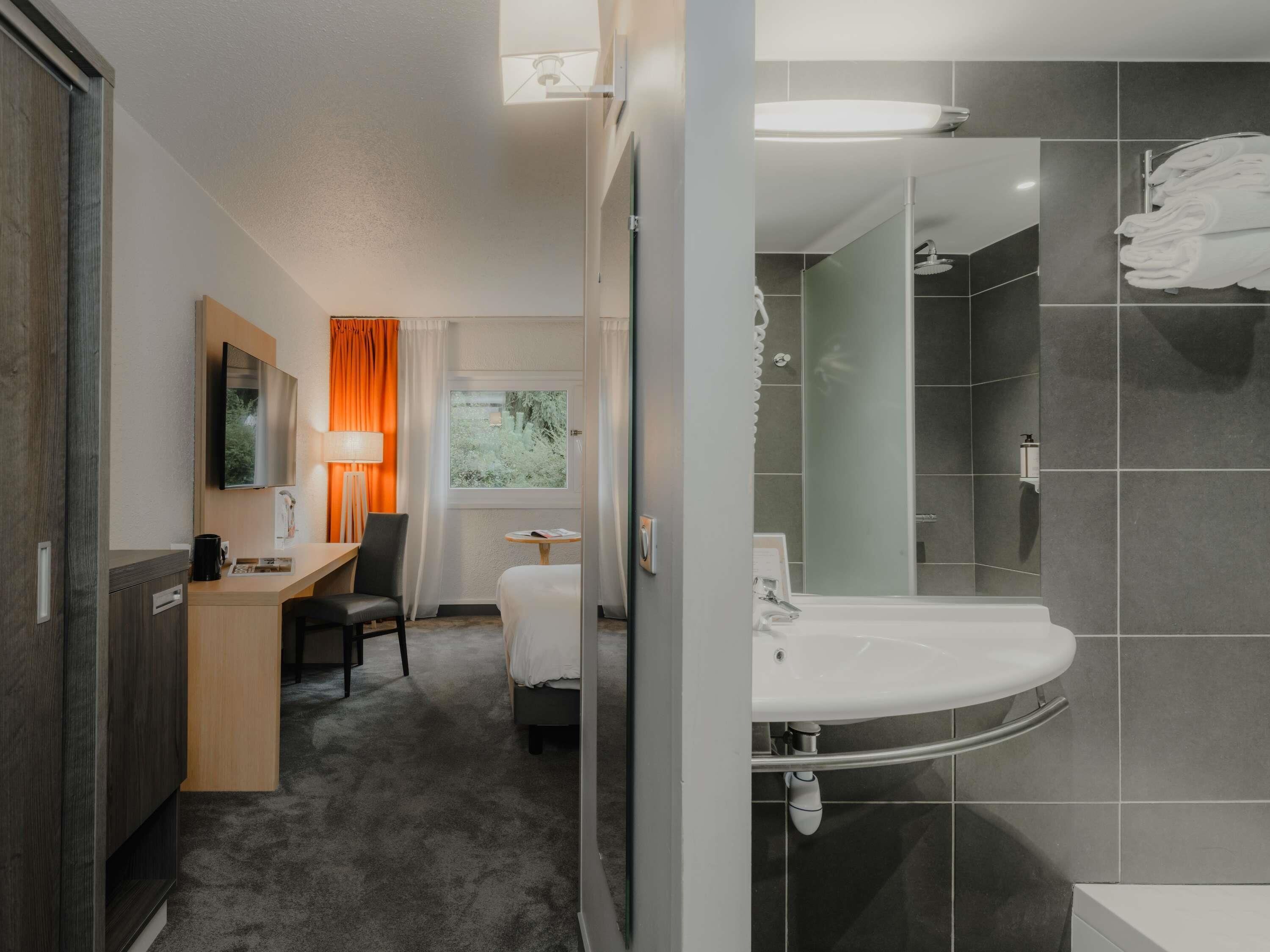 Una habitación de hotel con cama, escritorio, silla y baño con lavabo y ducha.