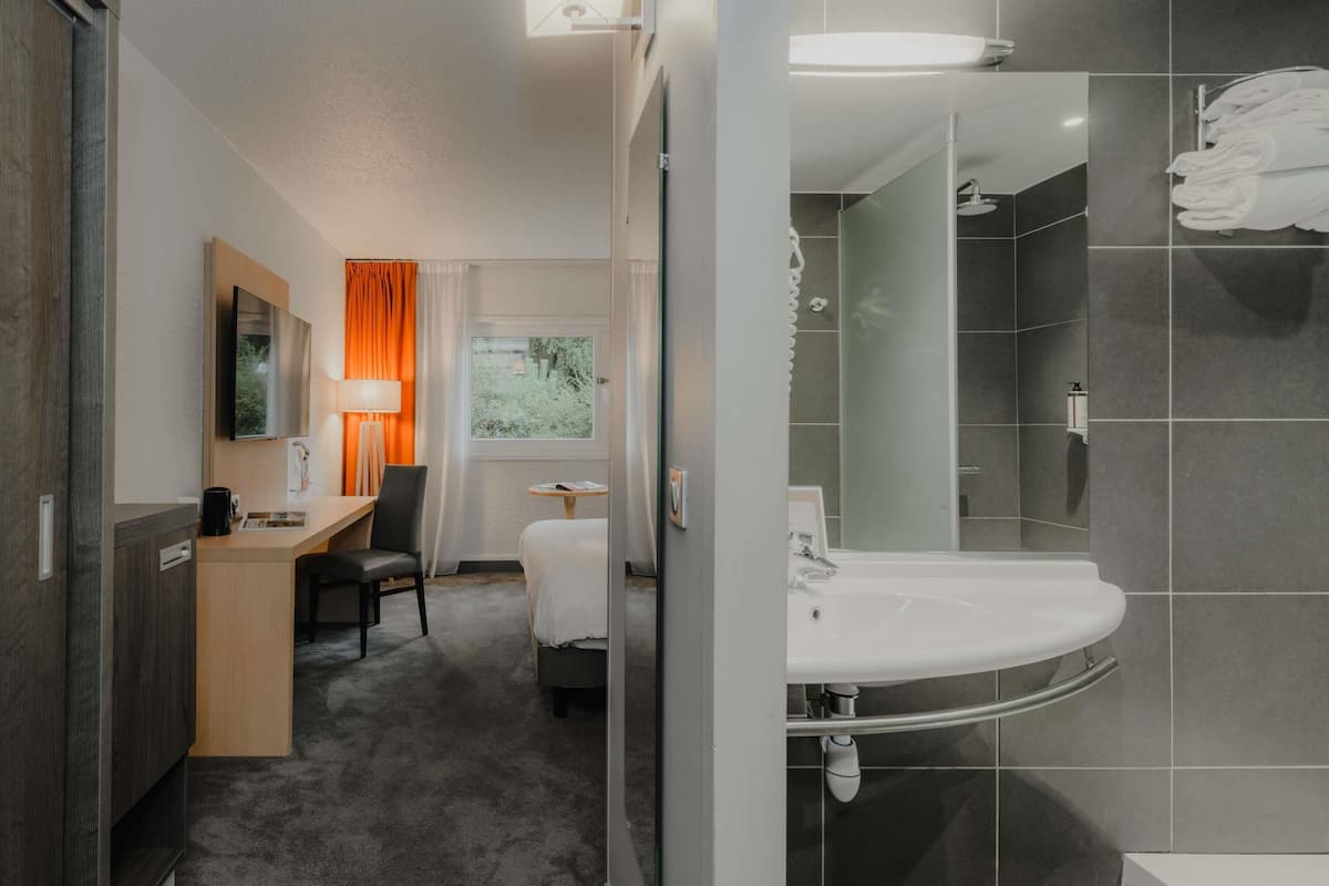 Una habitación de hotel con cama, escritorio, silla y baño con lavabo y ducha.