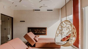 A modern living room with a large sofa, a hanging chair, and a fireplace. - Mercure Annecy Sud (Annecy)