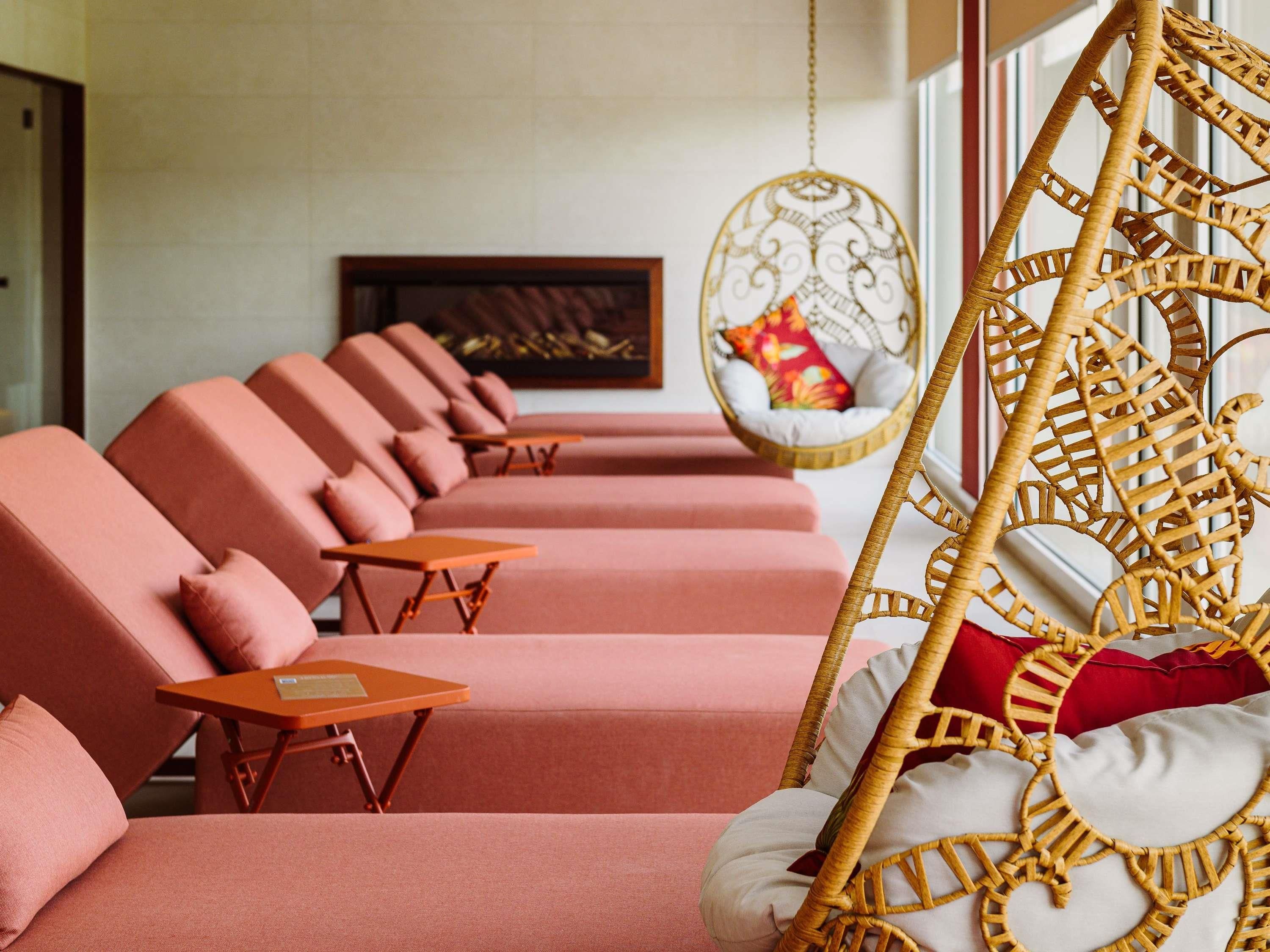 Una hilera de sofás rosados con mesitas pequeñas, un sillón colgante con asiento tejido y un cuadro enmarcado en la pared.