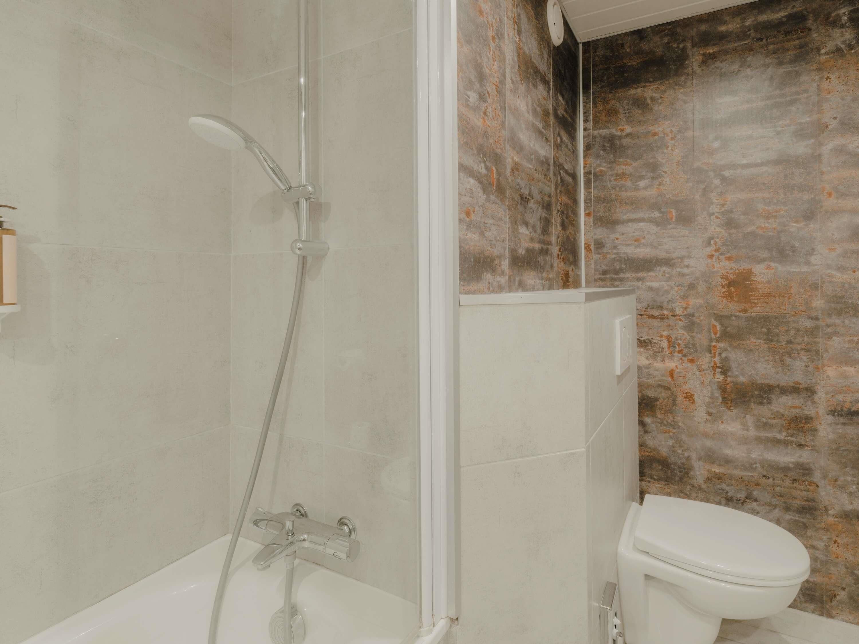 A bathroom with a shower, toilet, and a wall with a textured, rustic finish.