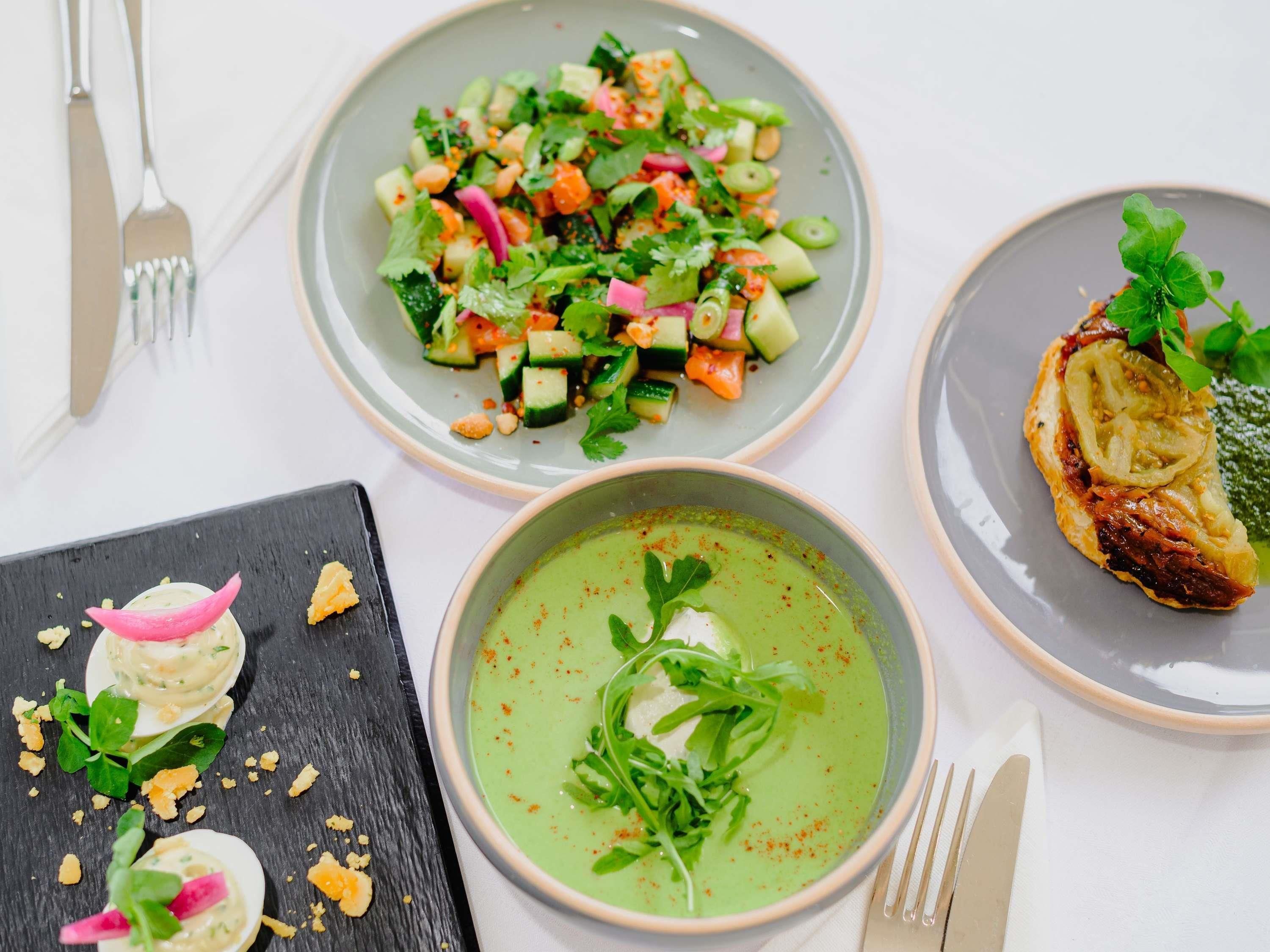 A table with three dishes: a salad, a soup, and a meat dish.