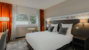 Una habitación de hotel con una cama grande, dos lámparas de noche, una mesita pequeña y una silla.