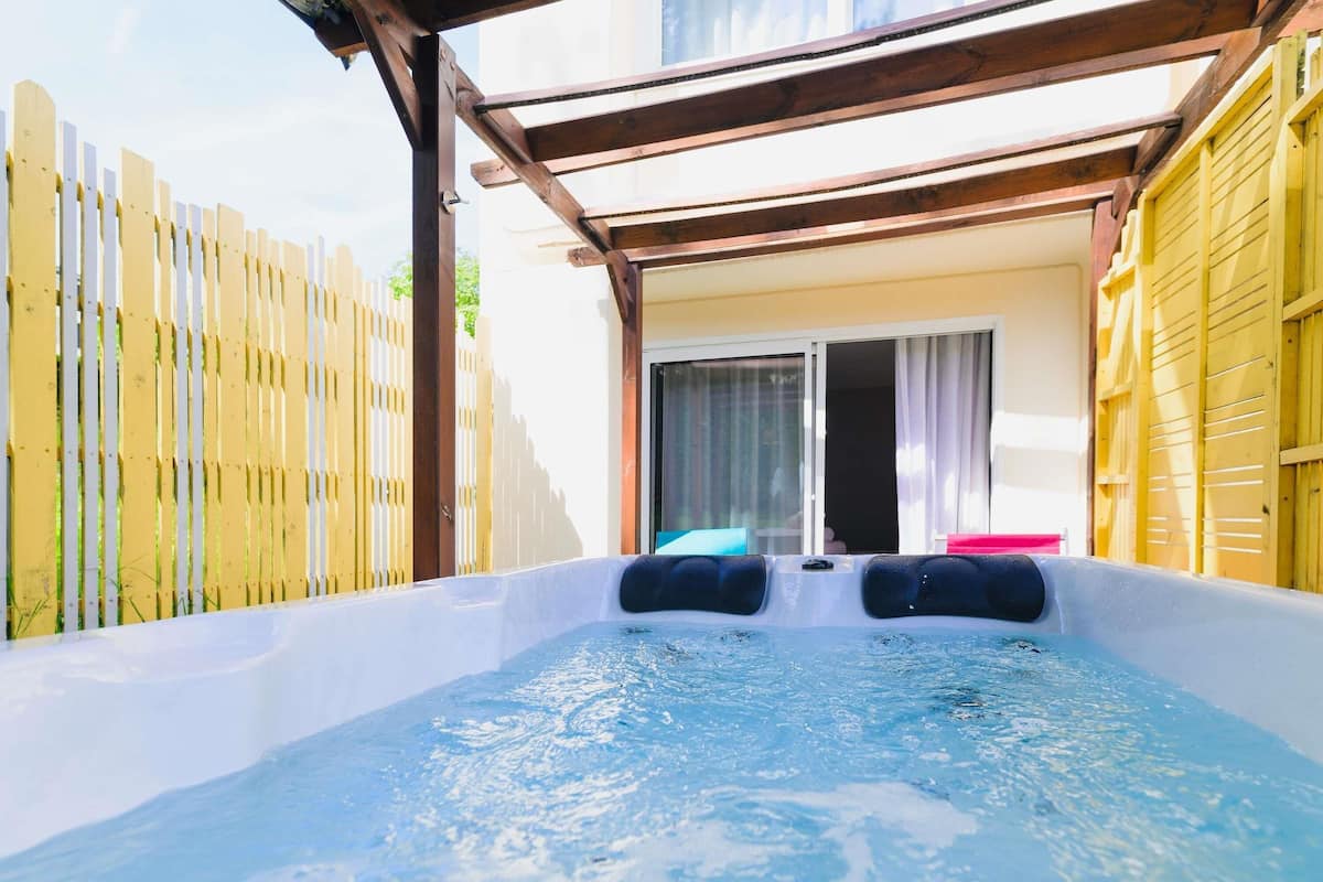 Un jacuzzi con dos asientos negros, una pérgola de madera y un ventanal corredero que da a una habitación.
