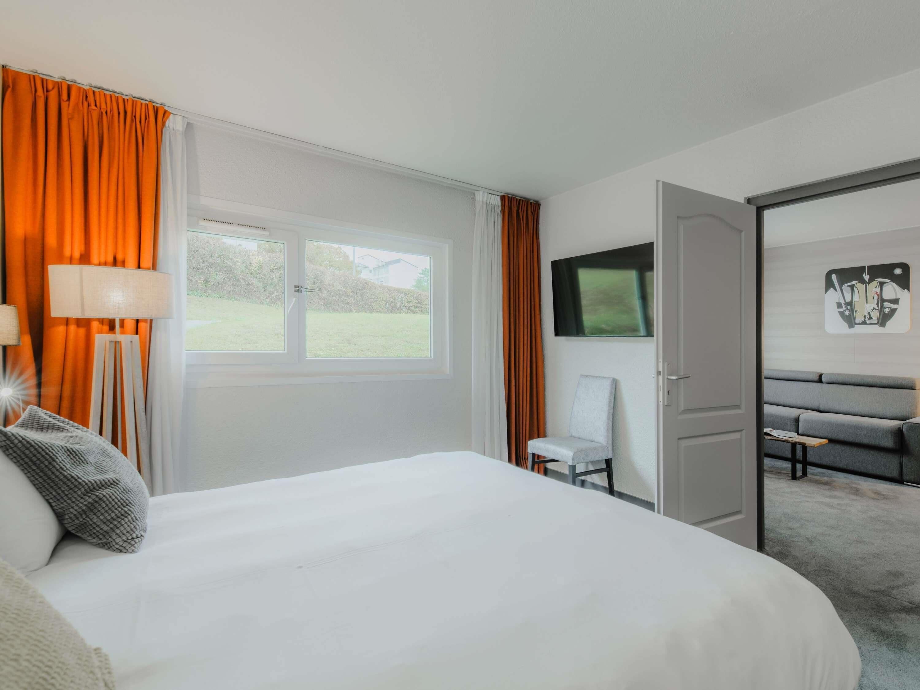 Ein Hotelzimmer mit einem großen Bett, einem Schreibtisch mit Stuhl, einem Fernseher und Blick ins Freie.