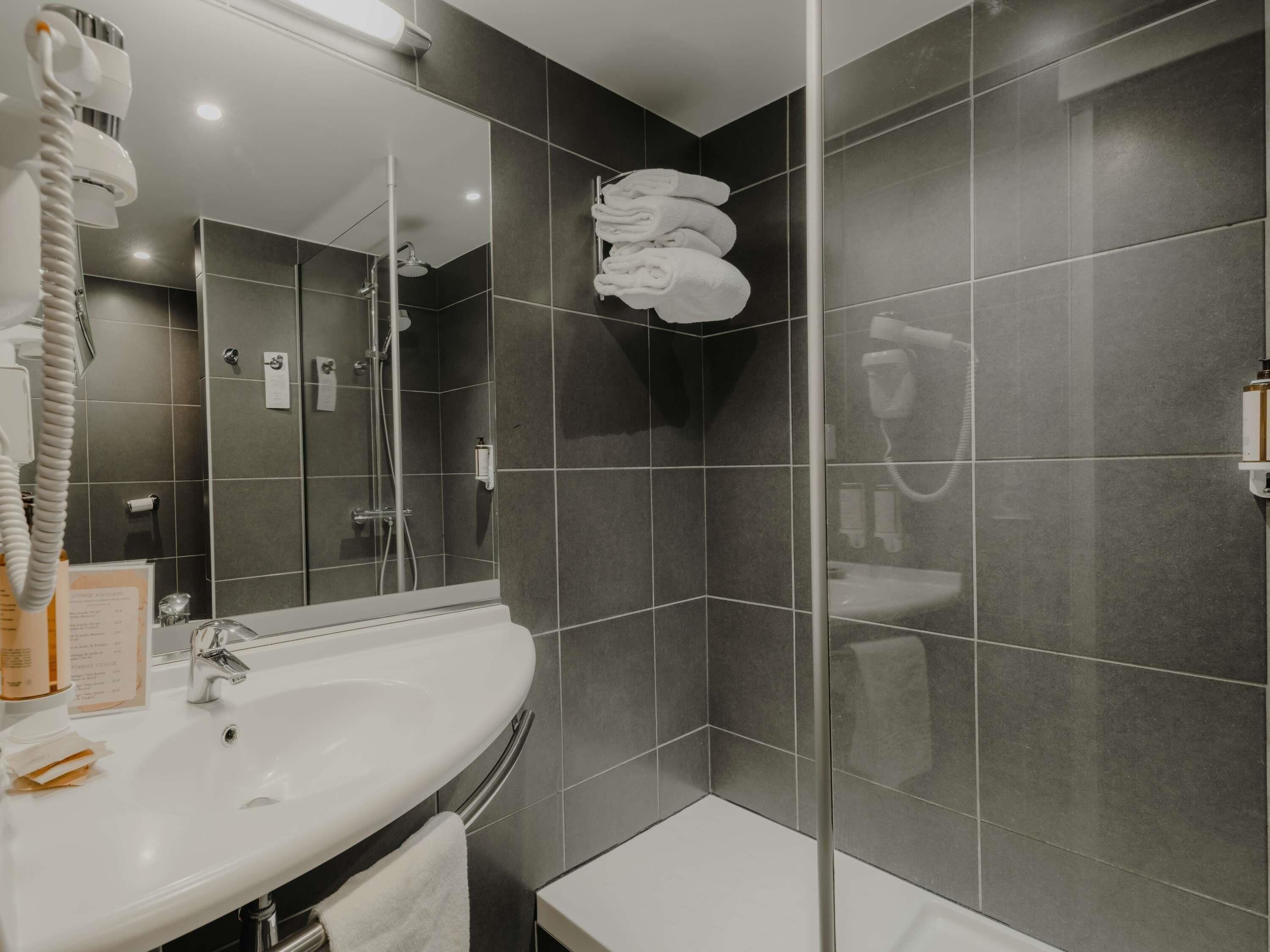 Un baño moderno con un lavamanos blanco, cabina de ducha con mampara de vidrio y un perchero con toallas dobladas.